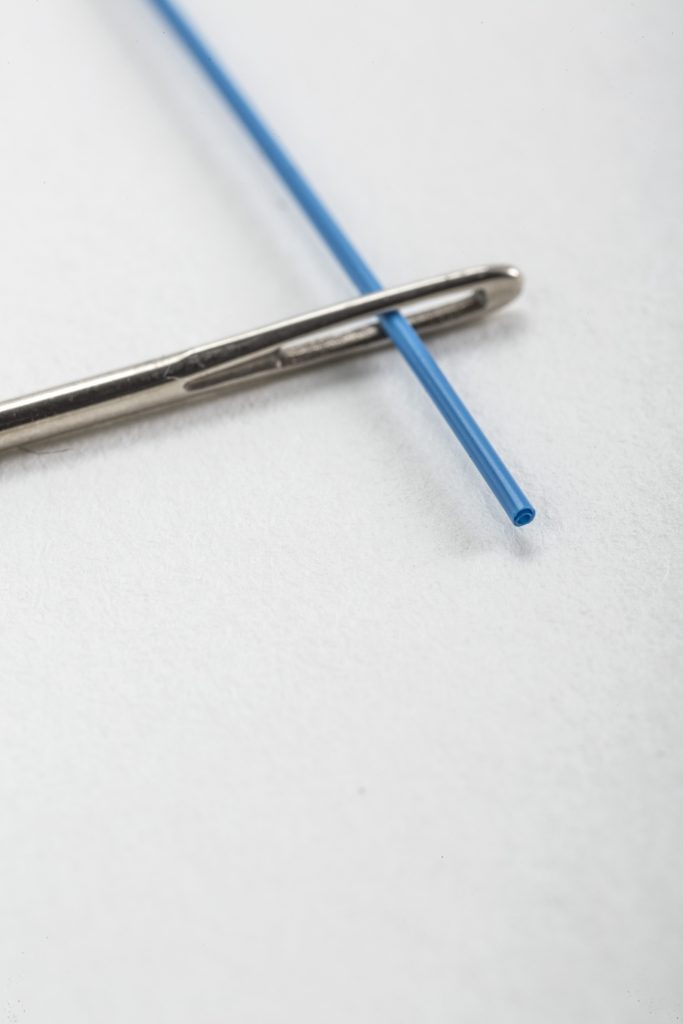 multi-lumen tube with cyclops design threaded through eye of a needle for size comparison