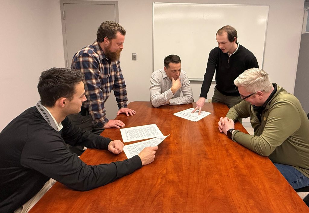 five male engineers around a table looking at documents