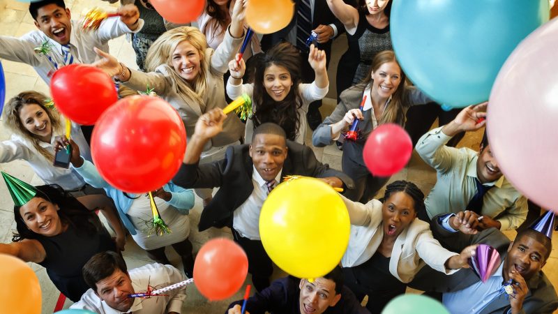 Business people having a party with balloons, hats and horns.